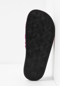 Semelle de sandale noire avec des motifs de bande de roulement hexagonaux et linéaires, vue en position verticale sur un fond blanc.