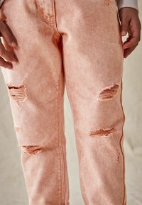 Jeans in denim rosa usurati con un taglio dritto, caratterizzati da strappi sulle ginocchia e sottili righe verticali nella trama del tessuto.