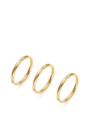 Tres delgados anillos de oro, cada uno con tres pequeños diamantes, dispuestos en diagonal sobre un fondo blanco.