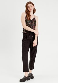 Camisole noire à motifs floraux avec un ourlet en dentelle associé à un pantalon noir taille haute. Le modèle porte des mocassins épais avec un détail en chaîne.