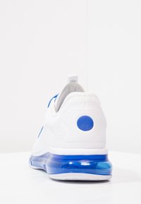 Vit sportig sneaker med blå accenter, ovandel i mesh, vadderad krage och en genomskinlig blå luftkuddesula. Påfallande logotyp på hälen.