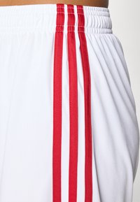 Witte sportieve shorts met rode zijstrepen, een elastische tailleband en een gladde, lichte stofstructuur.