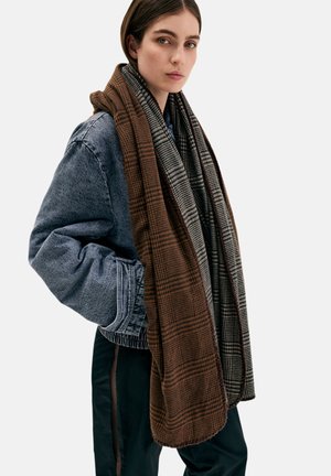 Braun-grau karierter Schal, geschichtet über einer Jeansjacke, mit weicher Textur und abgerundeten Kanten, in einem lässigen, übergroßen Design.