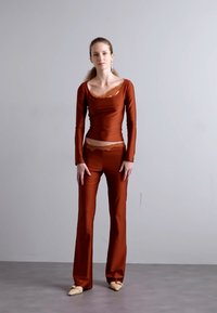 Bruine, lange mouwen top met kanten accenten, gecombineerd met bijpassende strakke broek, beide in een gladde stof. Het schoeisel van het model is in lichte kleur.