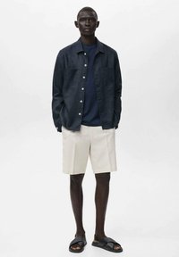 Mörkblå linnen skjorta med knappar, marinblå t-shirt, krämfärgade shorts och svarta sandaletter. Funktioner inkluderar en avslappnad passform och två bröstfickor.