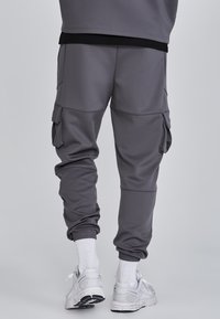 Grå joggebukser av mjukt material, med elastiska muddar, sidofickor och en avslappnad passform, parat med vita sportstrumpor och skor.