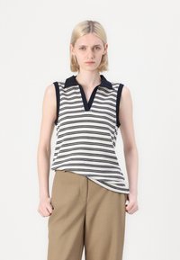 Gestreepte mouwloze top in crème en navy, met een V-hals en een contrasterende kraag. Gecombineerd met highwaisted beige broeken.