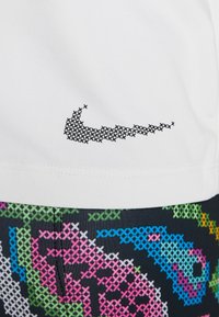 Wit shirt met korte mouwen en een zwart gestippeld Nike-logo, gecombineerd met kleurrijke, patroonrijke shorts met groene, roze en blauwe ontwerpen op een donkere basis.