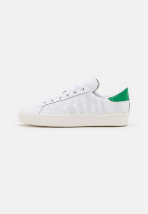 Sneaker bianca con parte superiore in mesh testurizzato, dettaglio verde sul tallone, lacci tondi e suola in gomma. Design semplice e a profilo basso.