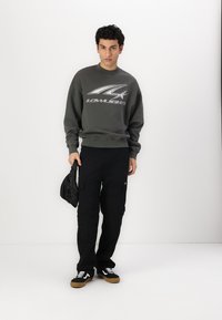 Gray sweatshirt with a metallic logo, paired with black cargo pants. Black sneakers with white accents and a small black bag.