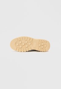 Suela de goma de color beige, con patrones circulares y tacos elevados para mayor tracción. Textura suave; robusta y diseñada para la durabilidad.