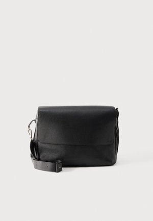 Sac à bandoulière noir en cuir grainé, avec un large rabat, une bandoulière réglable et des fermoirs argentés, sur fond clair.