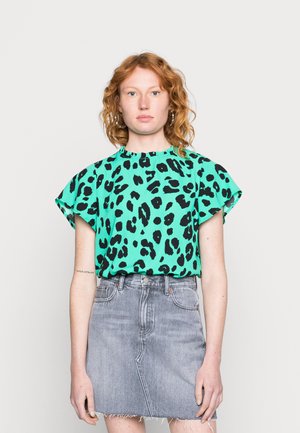 Blusa de estampa de leopardo verde com mangas curtas e decote cheio de volantes, acompanhada de uma saia mini de ganga cinza. Tecido texturizado, cores vibrantes.