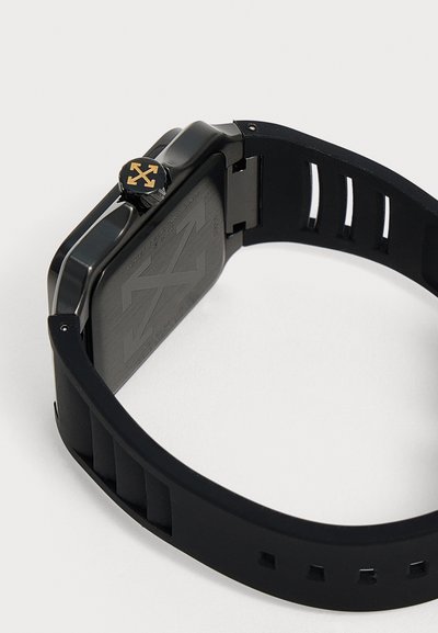 Montre-bracelet noire avec un cadran rectangulaire, un bracelet en caoutchouc noir et un logo flèche doré sur la molette de réglage latérale.