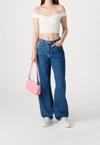 Bílý crop top s odhalenými rameny, modré široké džíny s květinovou výšivkou a růžová kabelka na rameno. Bílé tenisky doplňují celý outfit.