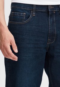 Tummansiniset farkut, joissa on tavallinen viiden taskun muotoilu, näkyvät saumat ja sileä pinta, jossa minimaalinen kulutus.