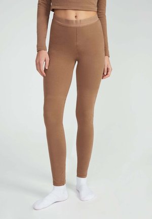 Leggings marroni aderenti realizzati in un tessuto elastico e liscio, con una vita alta e un design senza cuciture. Indossati con calzini bianchi alla caviglia.