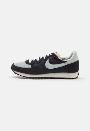 Czarny i jasnoszary sneaker Nike z białymi sznurowadłami, jasną podeszwą, widocznym logo swoosh oraz siateczkowymi detalami, pokazany z profilu na białym tle.