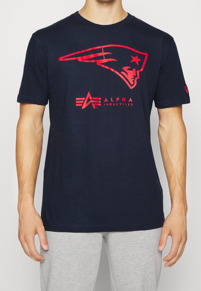 Námořnická modrá bavlněná tričko s červenou grafikou helmy a logem "Alpha Industries" v červené barvě pod ní. Krátké rukávy, kulatý výstřih.