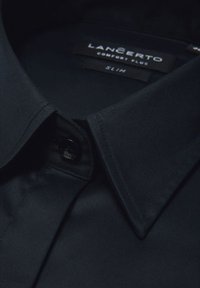 Ciemnoniebieska koszula z długim rękawem o dopasowanym kroju, gładkiej fakturze materiału, kołnierzyku zapinanym na guziki i metkach marki ukrytych wewnątrz kołnierza.