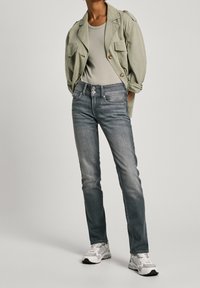 Světle zelená, texturovaná bunda přes přiléhavé šedé tílko; modrošed é džíny se dvěma knoflíky; bílé a šedé tenisky.