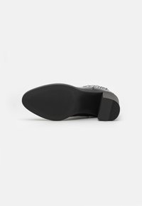 Semelle de chaussure noire avec une surface en caoutchouc texturée, présentant un léger talon et un motif strié pour une meilleure adhérence. Design minimaliste et forme compacte.