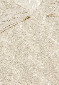 Top din tricot de culoare albă, cu un model texturat în dungi zigzag și țesătură deschisă. Material ușor, cu un aspect moale și ușor transparent.