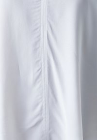 Vit tygblus med rynkad textur och en central söm. Slät material med en subtil lyster, utan synliga mönster eller dekorationer.