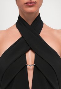 Top negru de tip halter cu material încrucișat la gât, având un accent circular argintiu în centru. Confecționat dintr-un material moale și texturat.