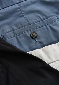 Poche en tissu bleu avec un bouton foncé, partiellement recouverte de couches de tissu noir et beige.