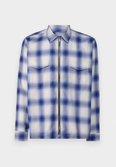 Ανοιχτό πουκάμισο από ελαφρύ ύφασμα με μπλε και λευκή καρό στάμπα, μακριά μανίκια, γιακά, δύο τσέπες στο στήθος και φερμουάρ μπροστά.