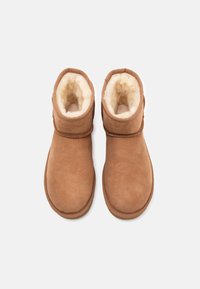 Brune ruskinds ankelstøvler med shearling-for, rund tå og justerbar kant. Designet til komfort og varme. Flad gummisål.