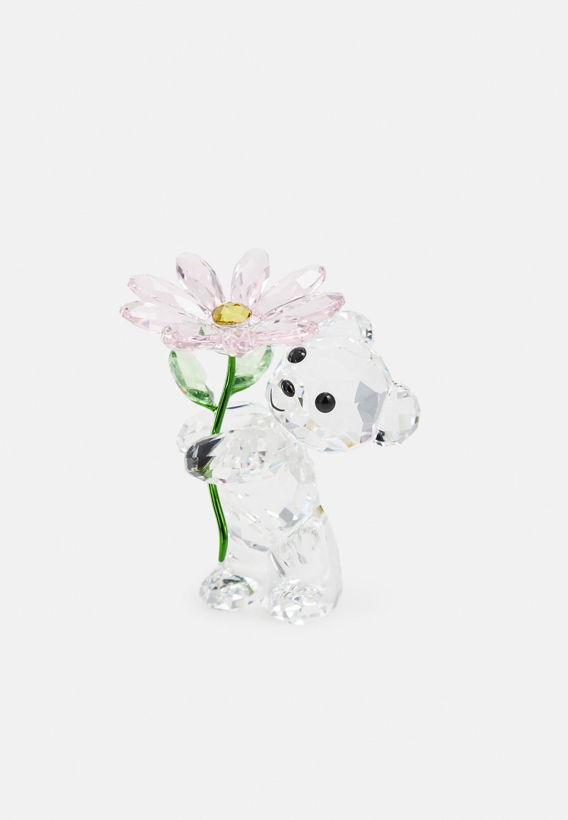 Urso de cristal transparente segurando uma flor rosa com folhas verdes. Detalhes notáveis incluem os olhos pretos do urso e a superfície facetada que confere brilho.