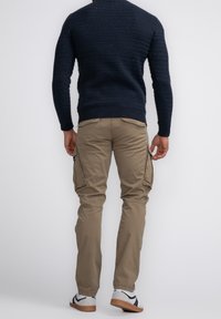 Kaki cargobyxor med flera fickor, tillsammans med en mörk marinblå texturerad tröja och grå sneakers med svarta accenter.