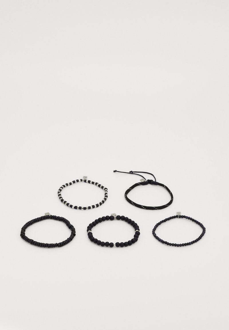Fem sorte perlekæder med varierede perleformer og et sort justerbart snorearmbånd arrangeret på hvid baggrund.