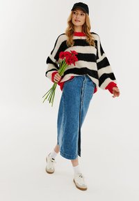 Pletený čierno-biely pruhovaný sveter s červenými akcentmi v kombinácii s modrou džínsovou maxi sukňou. Modelka drží červené kvety a má na sebe biele tenisky.