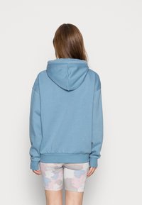 Felpa blu con cappuccio, realizzata in tessuto morbido, caratterizzata da una vestibilità comoda. Abbinata a pantaloncini chiari con fantasia.