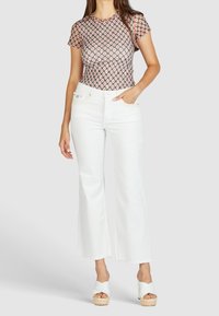 Mønstret kortærmet top i pink og sort, parret med hvide højtaljede flared jeans. Bemærkelsesværdig frynsekant og espadrille wedgesandaler.