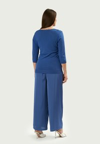 Maglione blu lavorato a maglia con maniche 3/4 e dettagli testurizzati sulle spalle, abbinato a pantaloni blu a gamba larga e sandali bianchi con tacco.