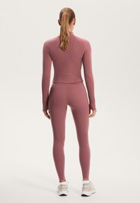 Form-fitting athletic wear in muted mauve, featuring long sleeves and leggings with fitted seams, made from smooth, stretchy fabric.