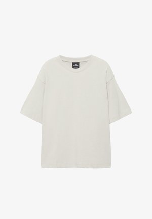 Lyse beige, oversized T-shirt med korte ærmer og rund halsudskæring samt synligt mærke indeni kraven på en hvid baggrund.