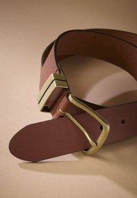Brown leather belt featuring a brass buckle and a rectangular accent. Smooth texture with a clean design and contrasting black edge stitching.
