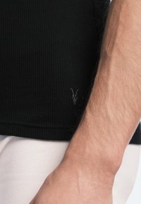 Schwarzes geripptes Tanktop mit enganliegendem Design. Verfügt über ein kleines gesticktes Logo am Saum. Die Textur ist glatt und flexibel.
