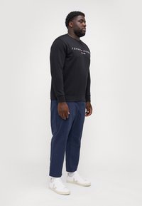 Black sweatshirt with "TOMMY HILFIGER" logo, paired with navy pants and white sneakers. The sweatshirt has a crew neckline and ribbed cuffs.