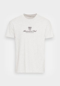 Camiseta de algodón gris claro con mangas cortas y escote redondo. Presenta un logo impreso más oscuro y texto en la parte frontal.