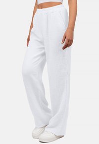 Witte, loszittende, gestructureerde broek van ademend materiaal met een elastische tailleband, gecombineerd met witte sneakers.