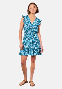 Blumenkleid in Blautönen mit Rüscheärmeln, V-Ausschnitt, elastischem Bund und ausgestelltem Rock. Trägt man mit braunen flachen Sandalen.