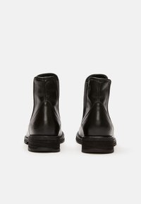 Botas de tobillo de cuero negro con un acabado suave, punta redondeada, paneles laterales elásticos y tacones bajos apilados. Diseño sencillo, sin logotipos visibles.