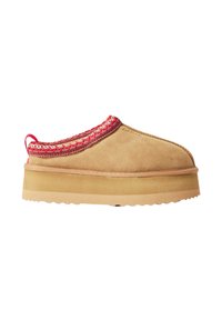 Scarpa slip-on in suede color tan con un accento rosso intrecciato attorno al colletto, caratterizzata da una suola piatta spessa e robusta con una finitura testurizzata.