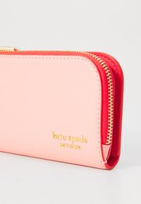 Ritsportemonnee in roze en rode synthetische materialen met een gestructureerd oppervlak. Kenmerkt een gouden logo en hardwaredetails langs de rand.